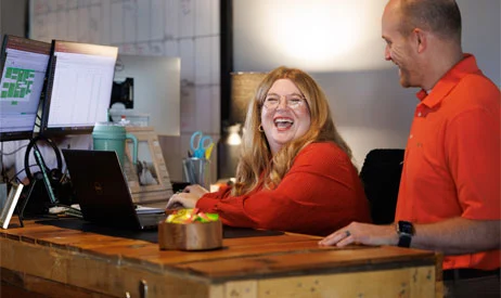 Two IT Company team members laughing together at a workstation